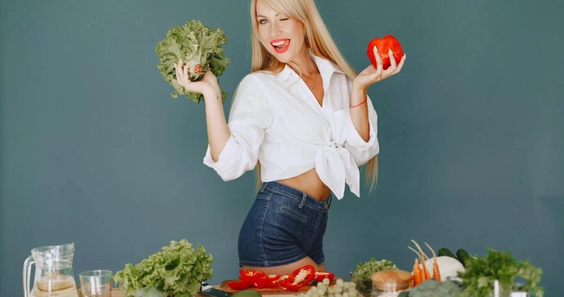 Cheerful woman in white shirt holding lettuce and pepper, celebrating fresh vegetables.